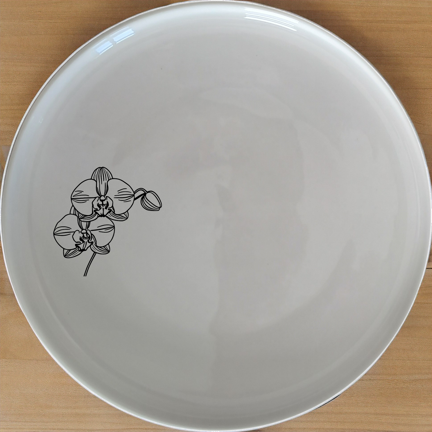 The Orchid Dinner Plate is a stunning addition to any dining set, featuring an elegant laser-etched orchid design on a sleek white ceramic surface.